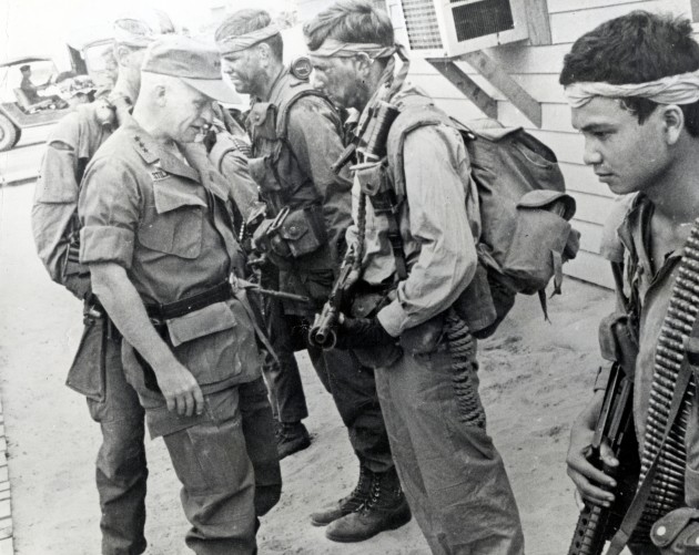 In April 1969, at CCN - the secret SOG compound in Da Nang, RT Idaho Green Beret Doug LeTourneau is queried by LTG Richard Stilwell, about a pending mission that RT Idaho was preparing to run in Laos. In the foreground is indigenous team member Cau, carrying 7.62 mm ammo for the M-60 machine gun and a CAR-15. To the right of LeTourneau is Capt. Michael O'Byrne. Stilwell inspected the team outside the CCN headquarters.  