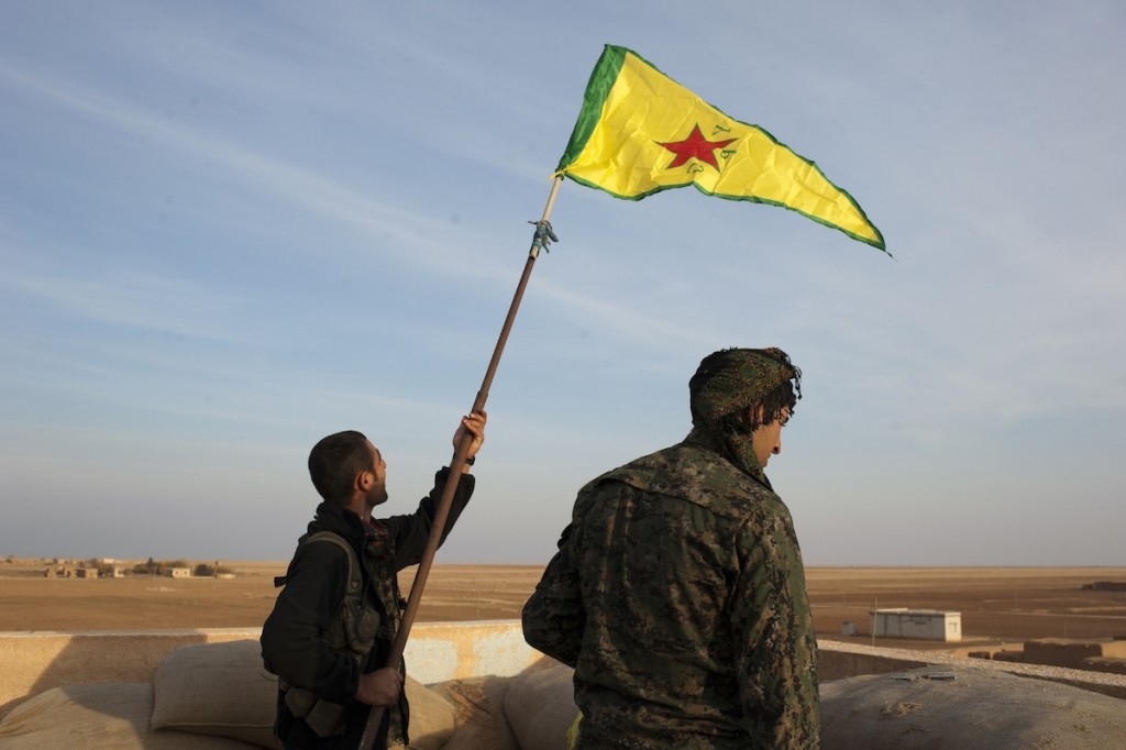 Two Kurdish fighters raise the flag of YPG on the roof of a building formerly occupied by ISIS, now under the control of YPG and YPJ near the frontline of Rabia, in Rojava, Syria, November 19, 2014.