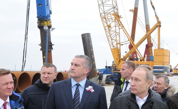 Russian President Vladimir Putin (R), accompanied with Russian head of Crimea Sergei Aksyonov (C) and head of the Federal Road Agency Roman Starovoit (L), inspects the site of the under-construction bridge across the Kerch strait, which will link Russia and the Crimean peninsula, on the island of Tuzla, on March 18, 2016. AFP PHOTO / SPUTNIK / MIKHAIL KLIMENTYEV / AFP PHOTO / Sputnik / MIKHAIL KLIMENTYEV