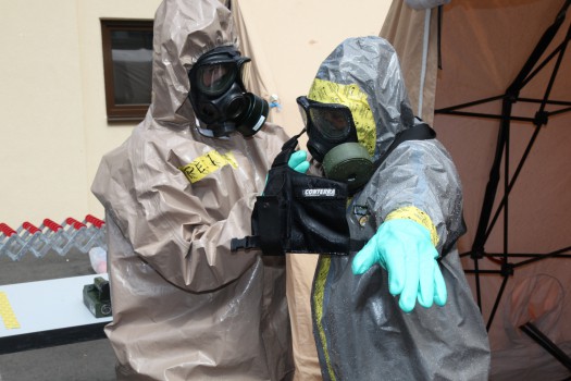 Sgt. Bajram Peci, left, leader decontamination station, 1st Platoon, Hazmat Company, Civil Protection Regiment, Kosovo Security Force, removes a chemical protection suit from Staff Sgt. Wendell Reeder, survey team chief, 773rd Civil Support Team, 7th Civil Support Command, and a native of Atlanta, during a Defense Threat Reduction Agency-sponsored preparedness partnership exercise on Panzer Kaserne