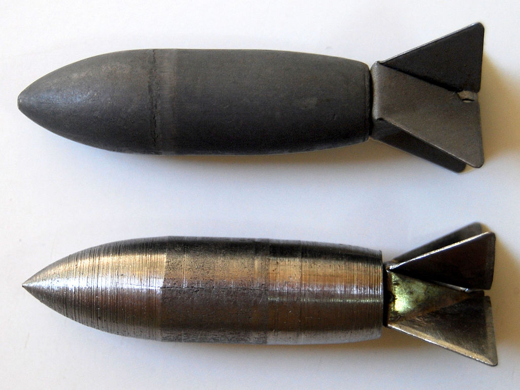 Photograph of 2 types of Lazy Dog Bombs: The top image shows an early WWII design which was forged from steel and given a Parkerized finish; the bottom image shows a later design which was manufactured on high-speed lathes from round steel rod stock and coated with cosmoline to prevent rusting during transport. Both had stamped and formed sheet metal fins spot welded to the tail end (Ikessurplus, CC BY 3.0 <https://creativecommons.org/licenses/by/3.0>, via Wikimedia Commons). Source: https://commons.wikimedia.org/wiki/File:Lazy_dog_bombs.jpg