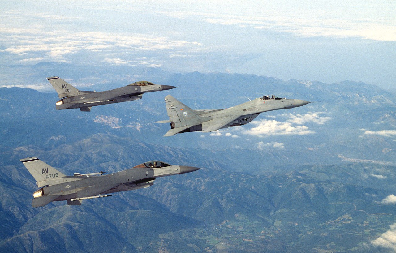 Two U.S. Air Force General Dynamics F-16C fighters from the 510th Fighter Squadron, 31st Fighter Wing, based at Aviano Air Base, Italy, fly in formation with a German Luftwaffe Mikoyan-Gurevich MiG-29A of the "Jagdgeschwader 73 (JG 73) Steinhoff" (73rd Fighter Wing), based at Laage, Mecklenburg-Vorpommern, Germany (photographer's name: SrA Tana R. Hamilton, USAF, Public domain, via Wikimedia Commons). Source: https://commons.wikimedia.org/wiki/File:USAF_F-16s_Luftwaffe_MiG-29_1995.jpeg