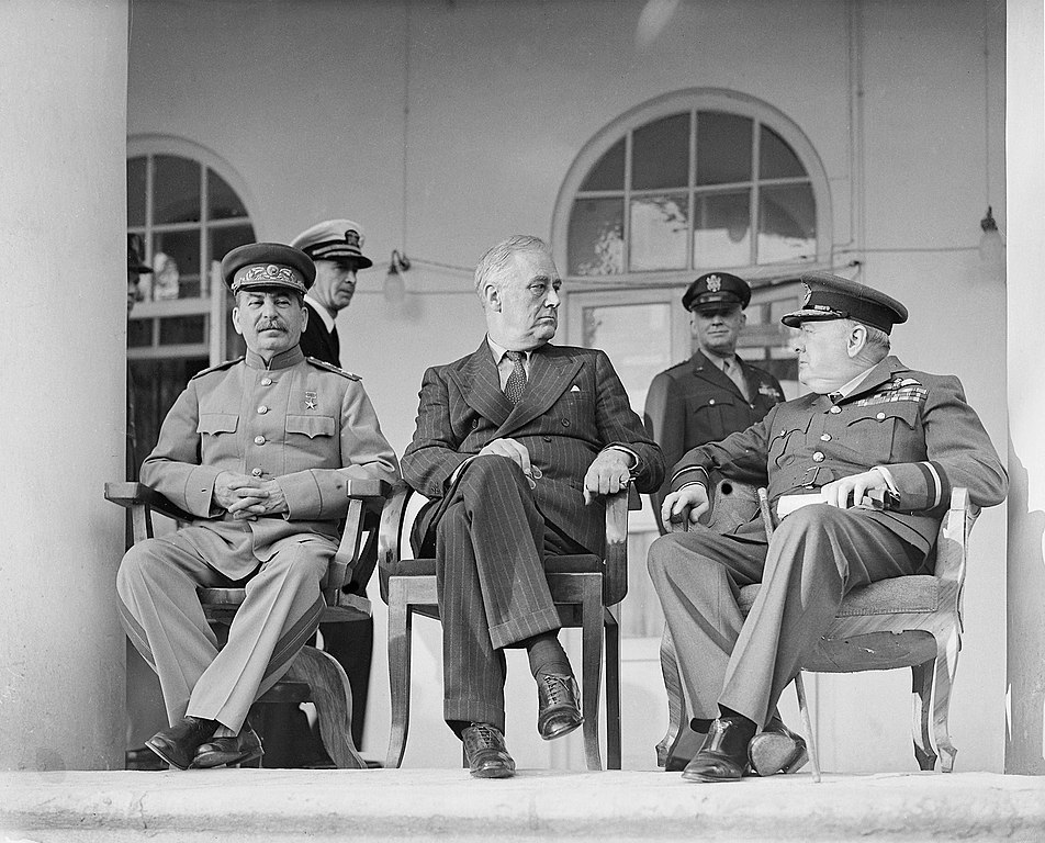 Joseph Stalin, Franklin D. Roosevelt and Winston Churchill on the veranda of the Soviet Legation in Teheran, during the first “Big Three” Conference, November 1943. In the background are aides to the US President (Oulds, D C (Lt), Royal Navy official photographer, Public domain, via Wikimedia Commons). Source: https://commons.wikimedia.org/wiki/File:Joseph_Stalin,_Franklin_D_Roosevelt_and_Winston_Churchill,_in_Teheran,_1943,_edit.jpg