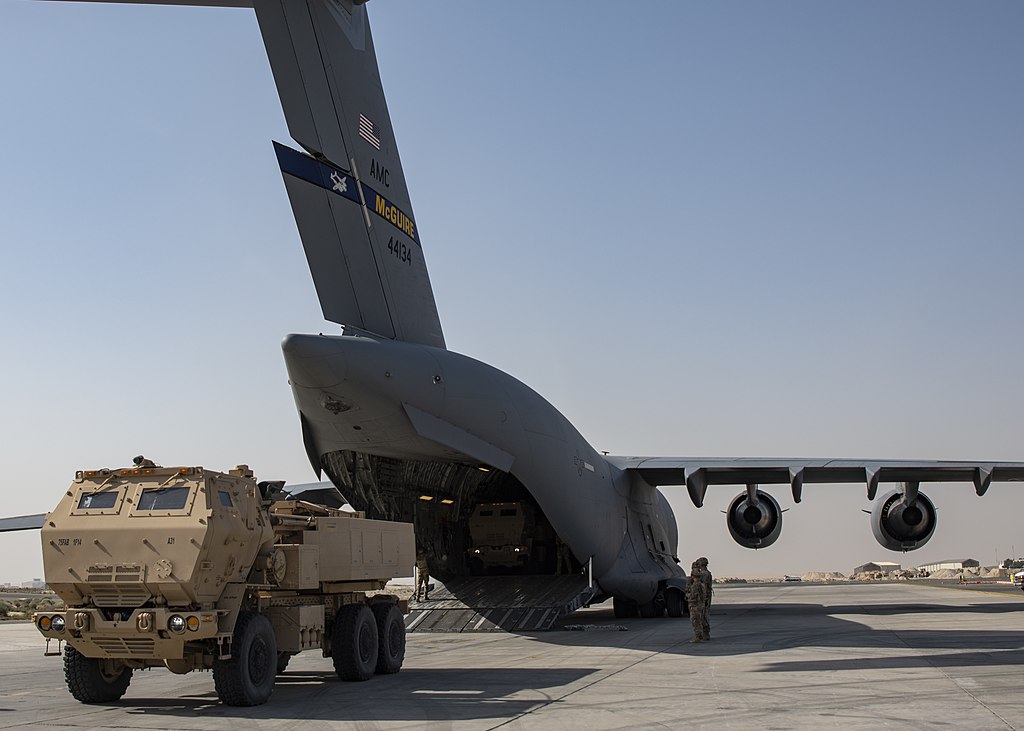 U.S. Army M142 High Mobility Artillery Rocket Systems assigned to the 1st Battalion, 14th Field Artillery Regiment are being loaded into a U.S. Air Force C-17 Globemaster III assigned to the 816th Expeditionary Airlift Squadron as part of joint training at Ali Al Salem Air Base, Kuwait, Jan. 27, 2021 (Senior Airman Kristine Legate, Public domain, via Wikimedia Commons). Source: https://commons.wikimedia.org/wiki/File:M142_HIMARS_-_210127-F-PV484-1022.jpg
