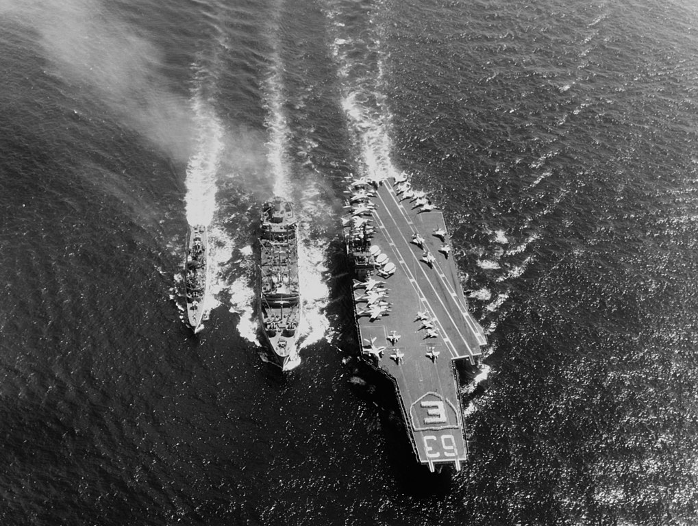 The U.S. Navy aircraft carrier USS Kitty Hawk (CVA-63) and the destroyer USS Turner Joy (DD-951) refueling from the fleet olier USS Kawishiwi (AO-146) on 23 April 1964. Note the large E in a shield spelled out by crewmen on the carrier's flight deck. Kitty Hawk, with assigned Carrier Air Wing 11 (CVW-11), was deployed to the Western Pacific from 17 October 1963 to 20 July 1964 (PHCS Brown, U.S. Navy, Public domain, via Wikimedia Commons). Source: https://commons.wikimedia.org/wiki/File:USS_Kitty_Hawk_(CVA-63)_and_USS_Turner_Joy_(DD-951)_refueling_from_USS_Kawishiwi_(AO-146)_on_23_April_1964.jpg