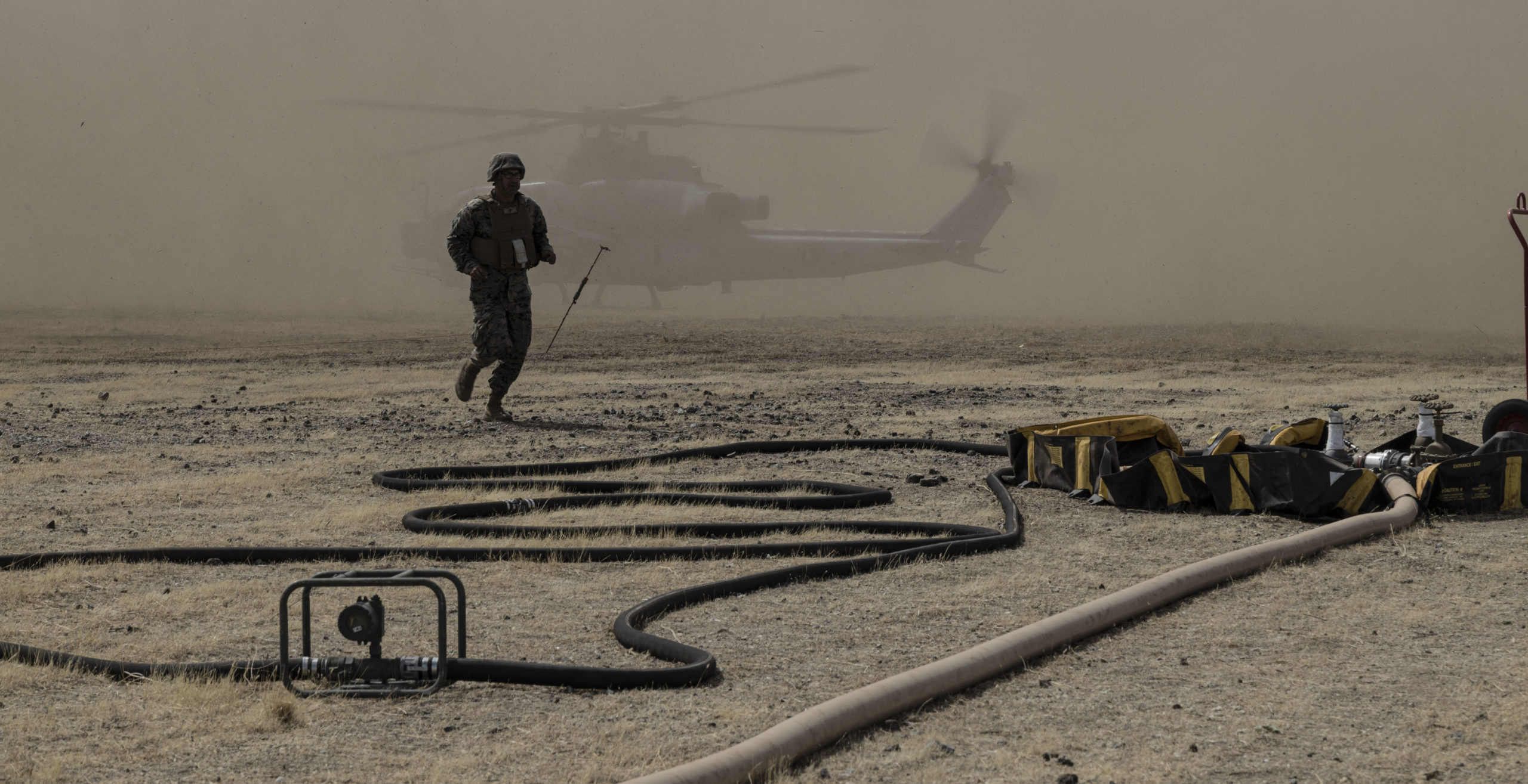 A man running, behind is a MACG-38 AH-1Z Viper in dust clouds
