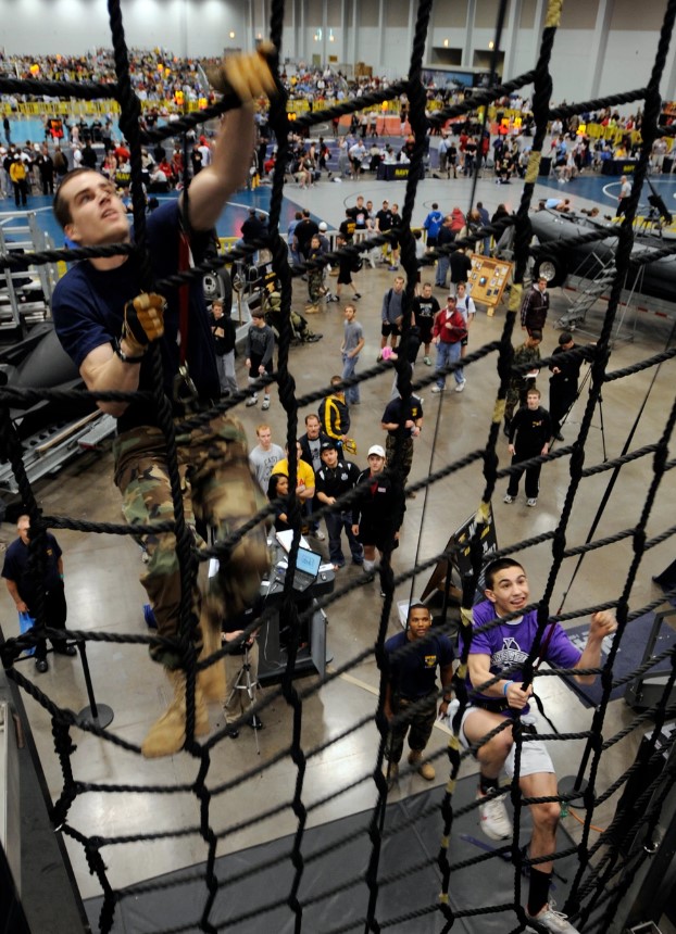 A high school wrestler challenges a member of the special warfare community to a race up the cargo net at the Navy SEAL Accelerator during the National High School Wrestling Championships at the Virginia Beach Convention center. The accelerator offered high school wrestlers from around the country the opportunity to see some of the career choices the Navy has to offer. (Source: US Navy)