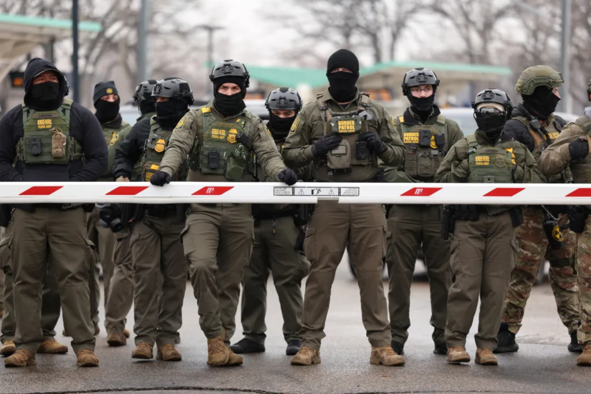 U.S. Border Patrol agents wearing tactical gear and face coverings stand behind a security barrier outside the Bishop Henry Whipple Federal Building in Minneapolis on Jan. 8, 2026.