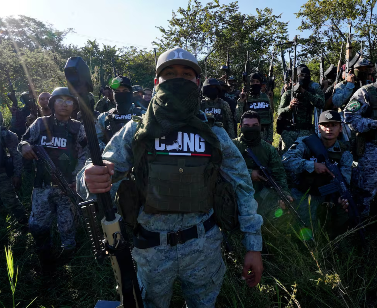 Armed members of the Lagarto Operational Group, an armed wing of the Jalisco New Generation Cartel, standing in a wooded area with rifles and tactical gear, November 2023.