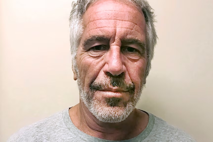 Headshot image of Jeffrey Epstein with gray hair and beard, wearing a gray shirt against a plain background.