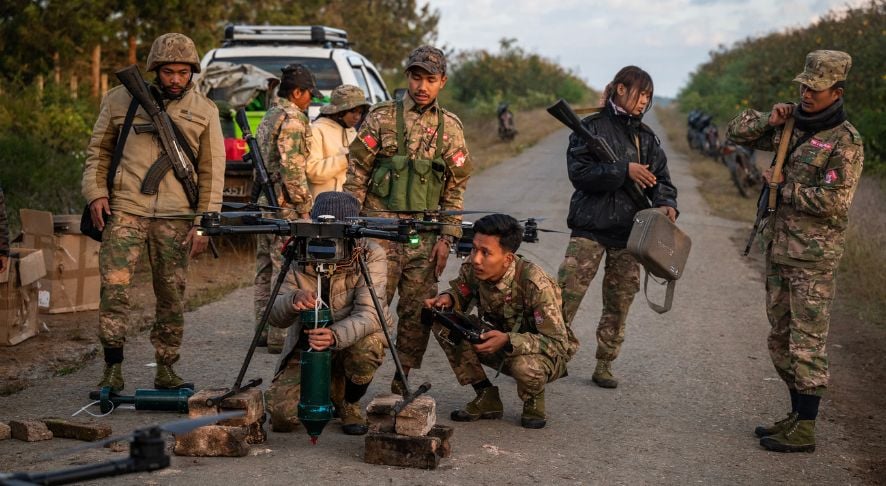 Myanmar soldiers in camouflage uniforms prepare and operate a large drone mounted on a launch stand along a rural road.