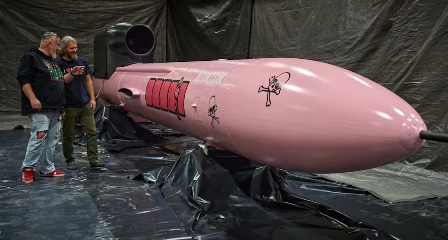 Two men stand beside a large pink Flamingo cruise missile inside a factory facility in Ukraine